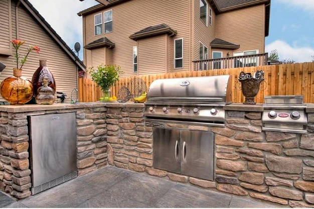 Custom home outdoor kitchen with a refrigerator, grill, and decorations on top of the counters