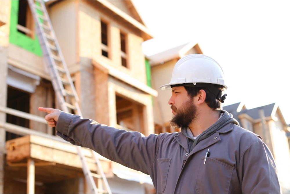 Construction worker wearing a hard hat and pointing towards a building under construction.