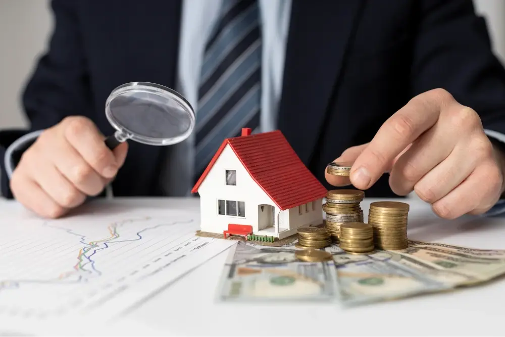 Magnifying glass over house model and coins.