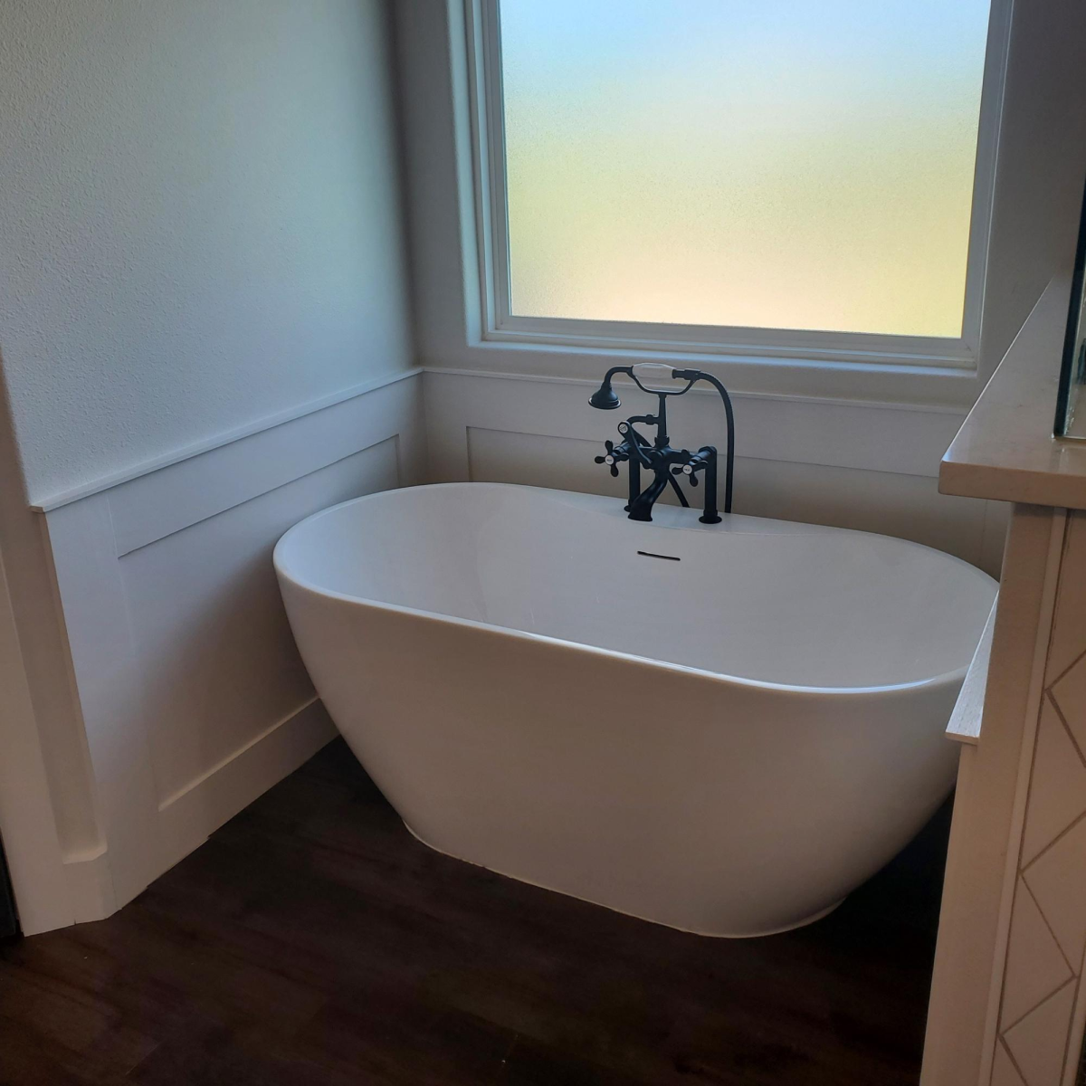 A sleek white freestanding bathtub with vintage black fixtures next to a frosted window.