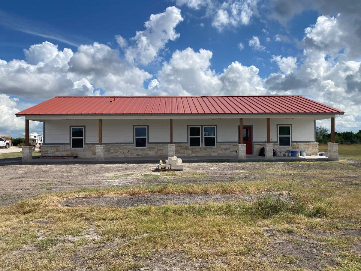 A modern ranch-style home with a red metal roof and stone accents under a bright sky.