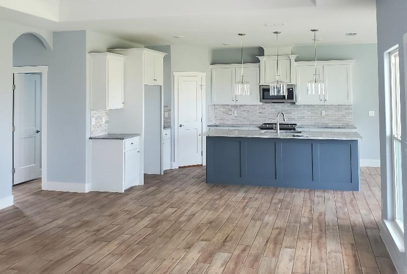 A spacious kitchen with white cabinets, a navy-blue island, and wood flooring.